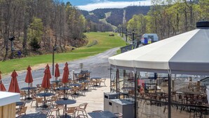 Una terraza con asientos al aire libre, con vistas a un valle boscoso y una pista de esquí.