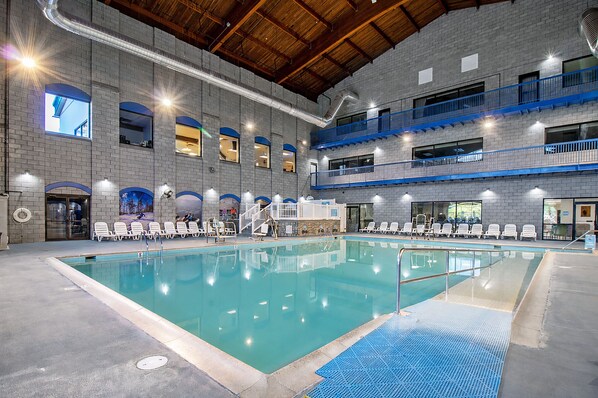 An indoor swimming pool with multiple levels of balconies, a brick wall, and a clear pool area.