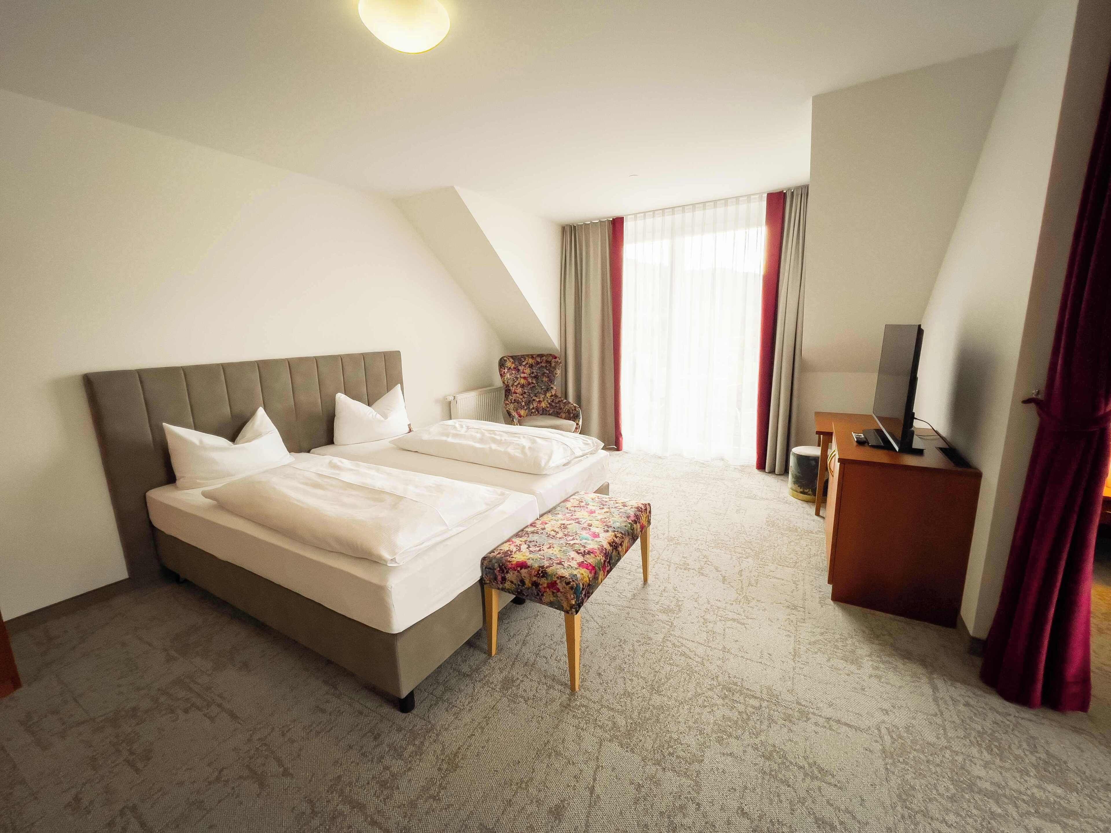 Une chambre d’hôtel avec un grand lit, un bureau avec un ordinateur, une chaise et une fenêtre avec des rideaux.
