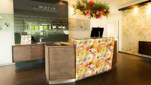 Een receptiebalie in een hotel, versierd met een bloemendesign, een welkomstbord en een grote bloemstelling erboven.