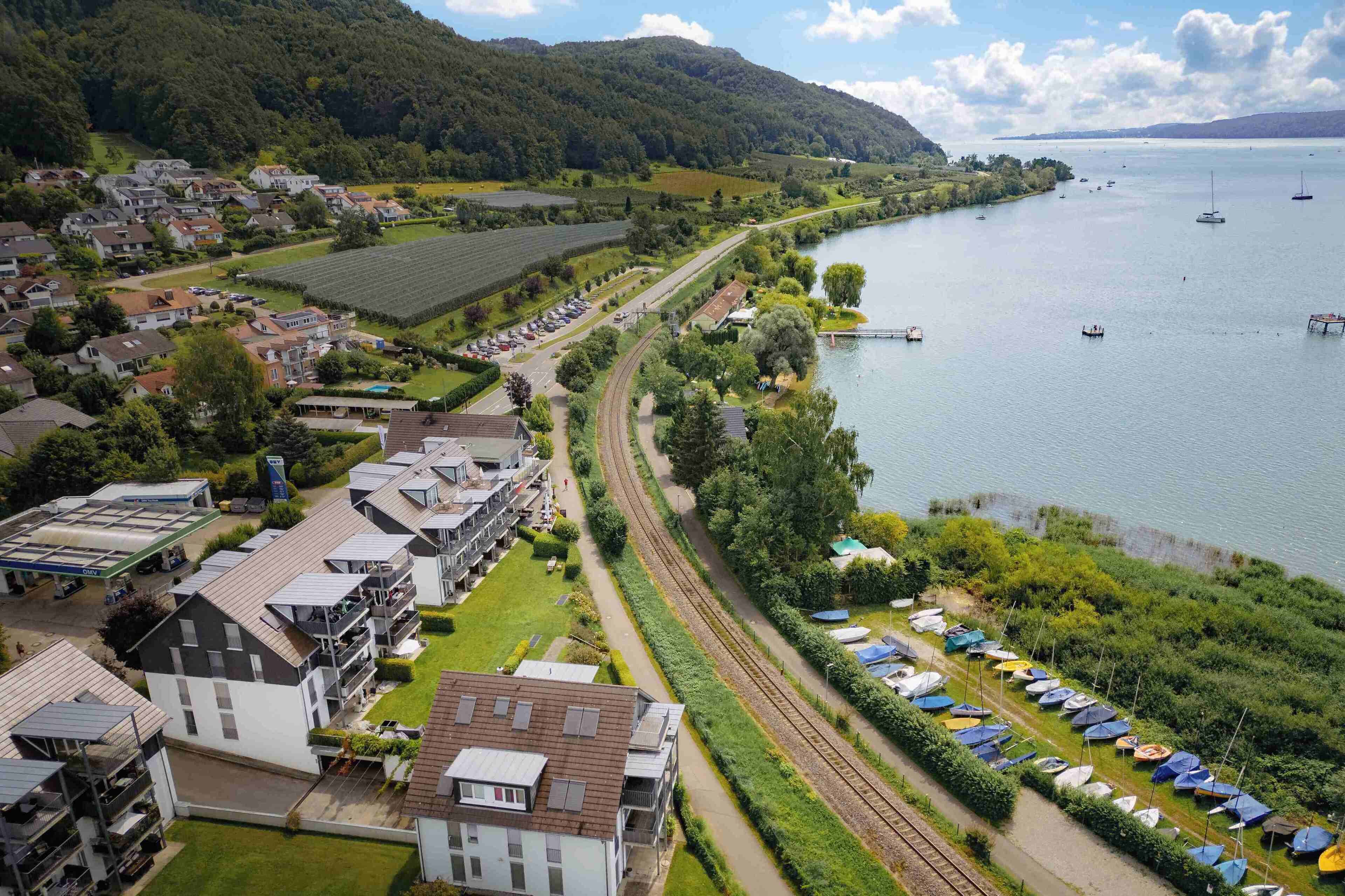 A lakeside town with residential buildings, a railway track, and a row of boats.
