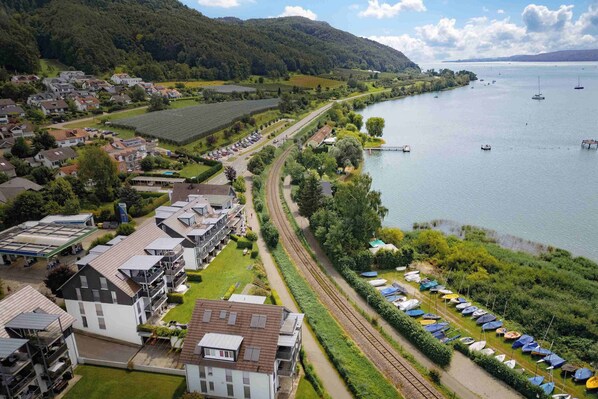 A lakeside town with residential buildings, a railway track, and a row of boats. - Hotel Rosmarin (Bodman-Ludwigshafen)