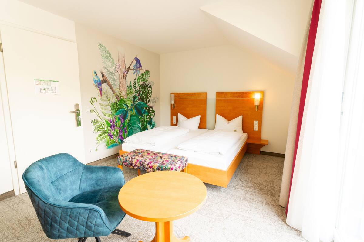 Een hotelkamer met een bed, een blauwe stoel, een klein tafeltje en een decoratieve plant.
