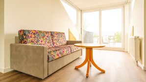 Een woonkamer met een bank, een ronde houten tafel en grote ramen.