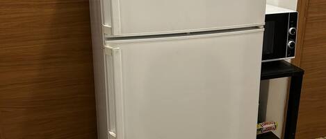 A white Bosch refrigerator in a kitchen with a wooden door and patterned floor tiles.