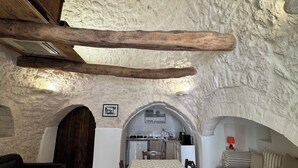 Een rustiek interieur met een stenen muur, houten balken, een eettafel met stoelen, een bank en een keukenhoek.