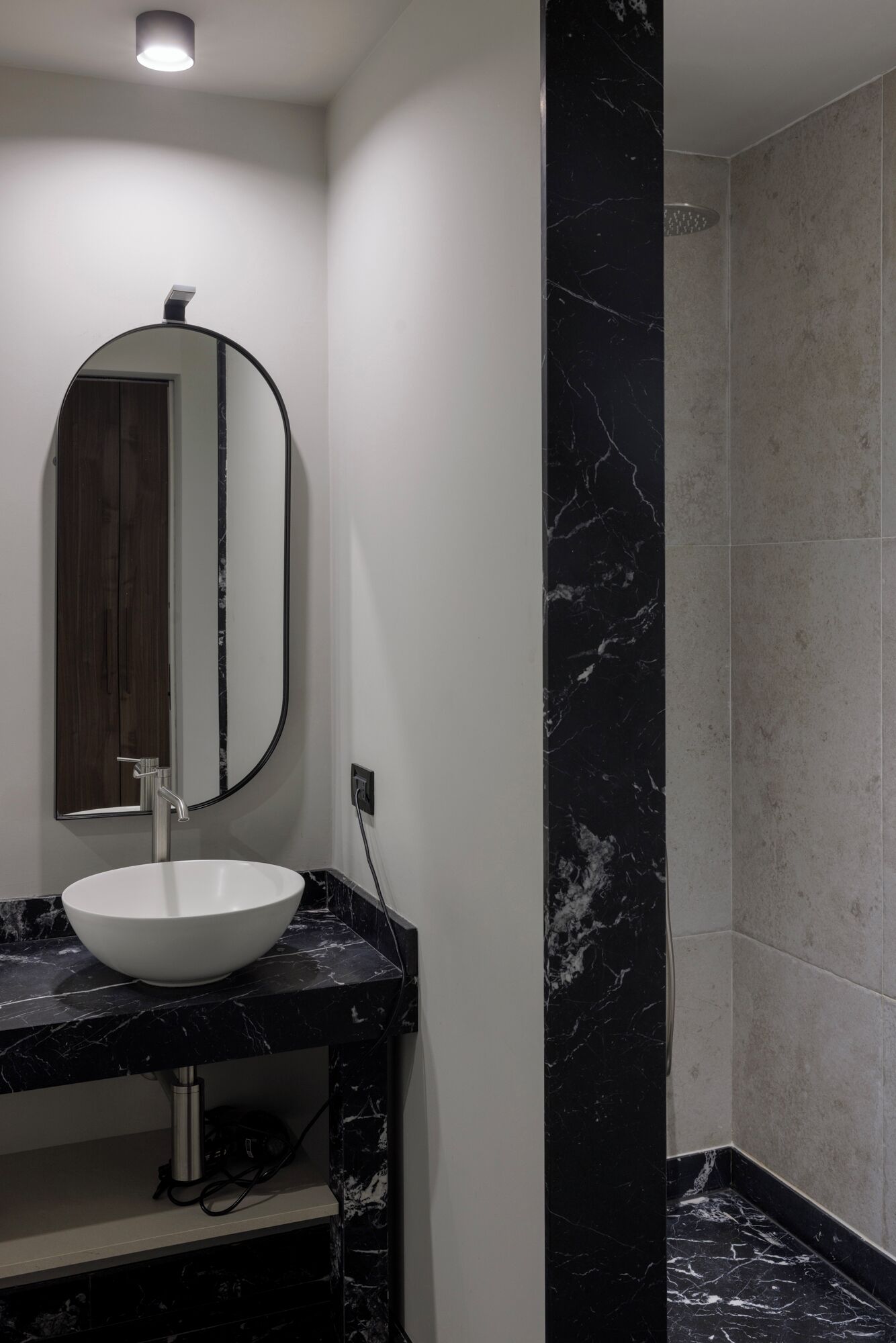 A modern bathroom with a white sink, a large mirror, and a shower area.