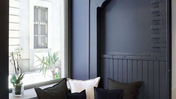 Un interior moderno con una pared azul oscuro, un banco acolchado con cojines y lámparas colgantes.