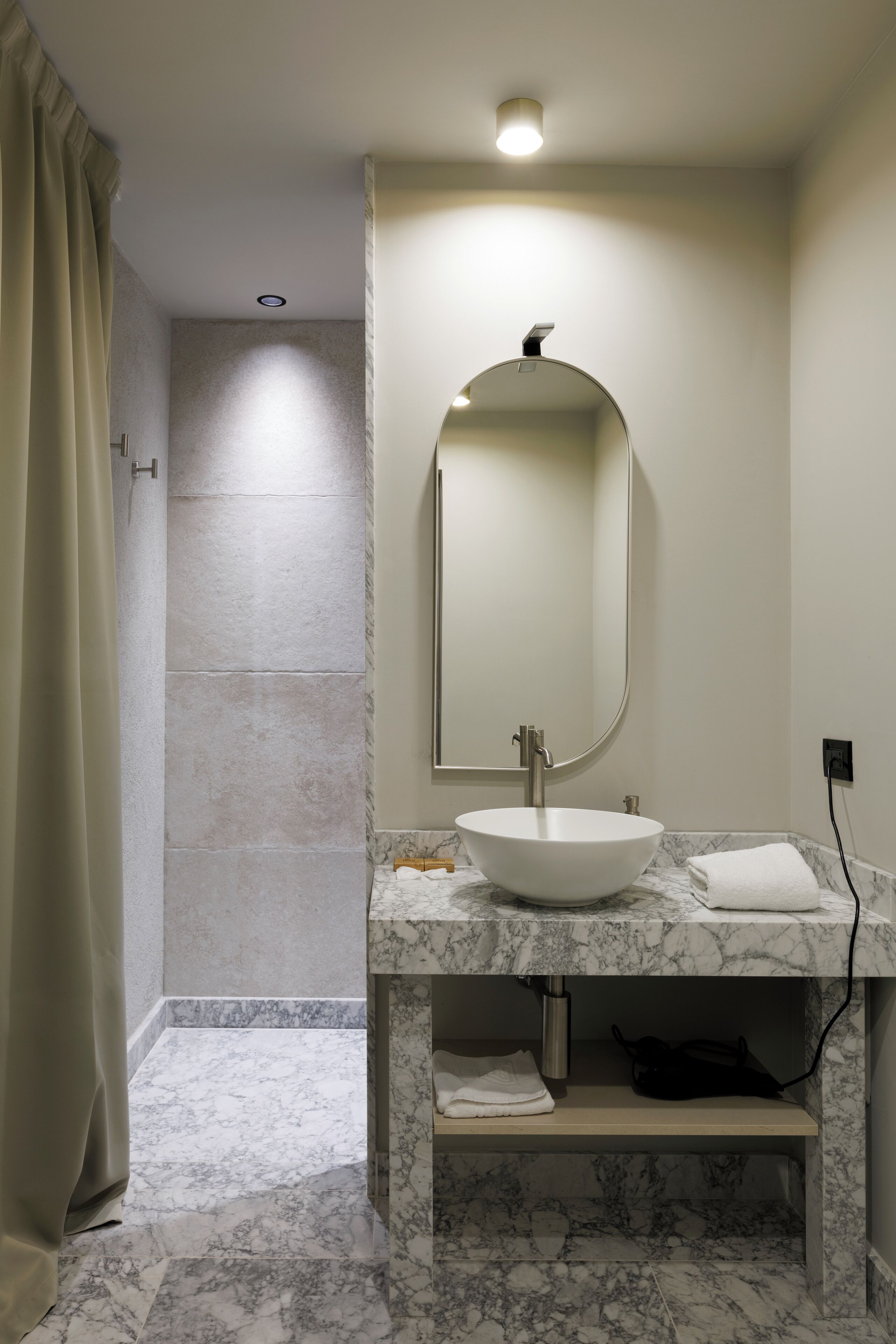 A bathroom with a marble sink, a mirror, and a shower area.