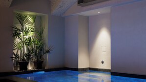 Una piscina interior con un elemento acuático azul, rodeada de paredes blancas y un techo de ladrillo.
