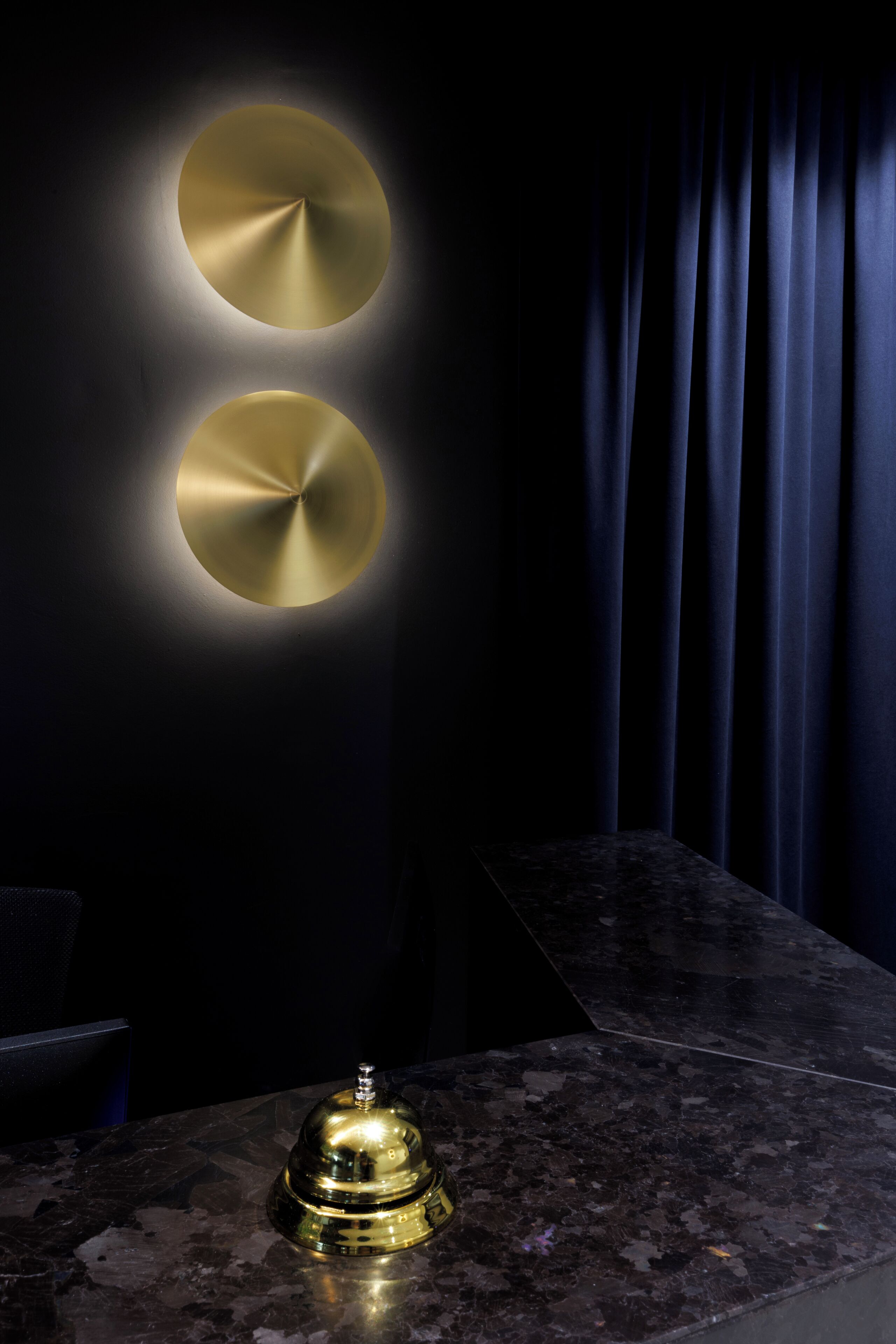 A dark room with two wall-mounted circular light fixtures and a bell on a marble counter.