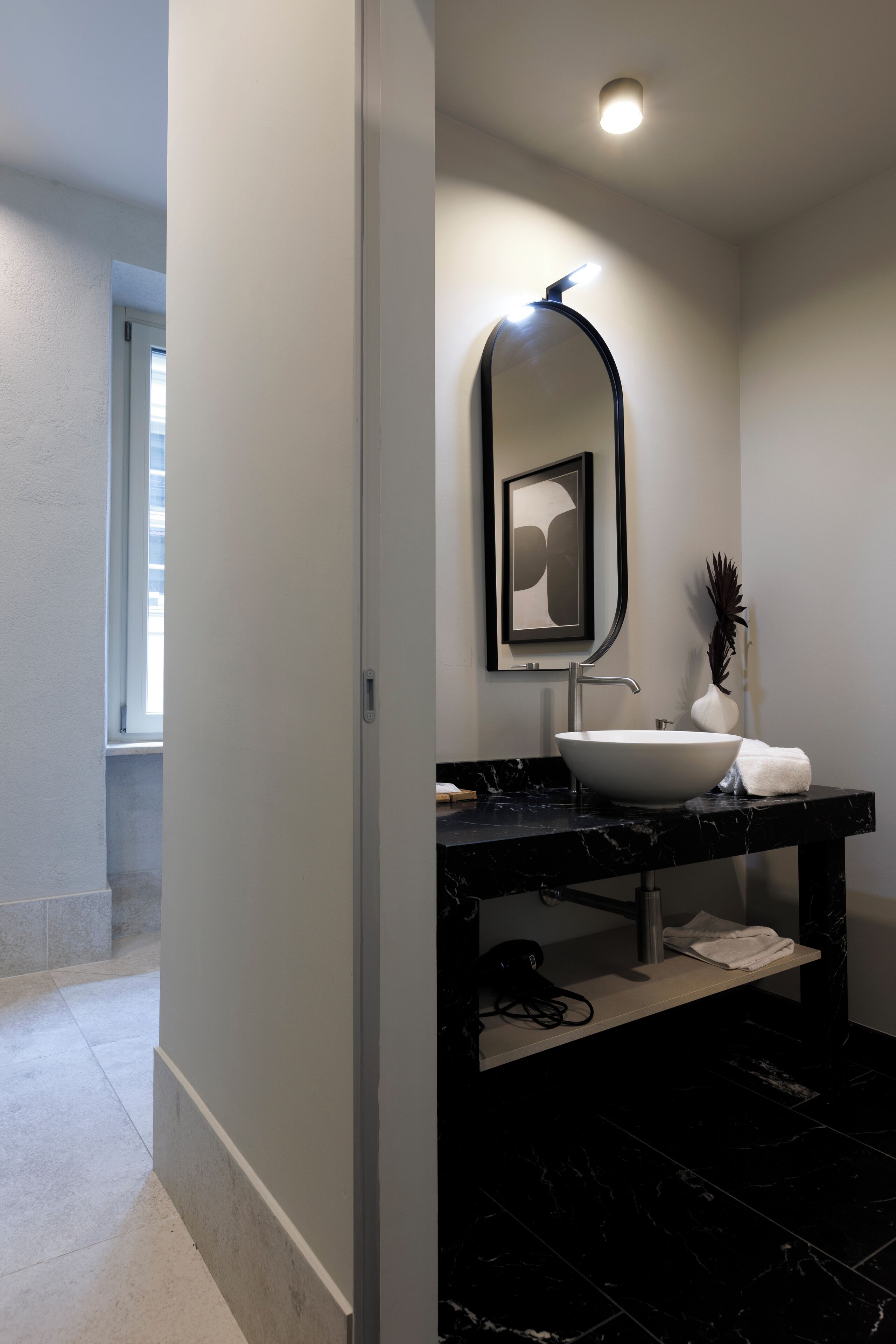 A modern bathroom with a white sink, black marble countertop, and a mirror with a black frame.