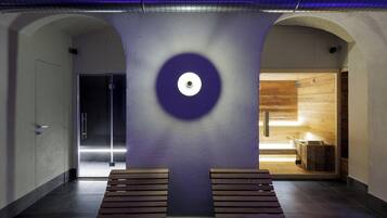 Un interior moderno con una lámpara circular central, bancos de madera y una zona de sauna visible.