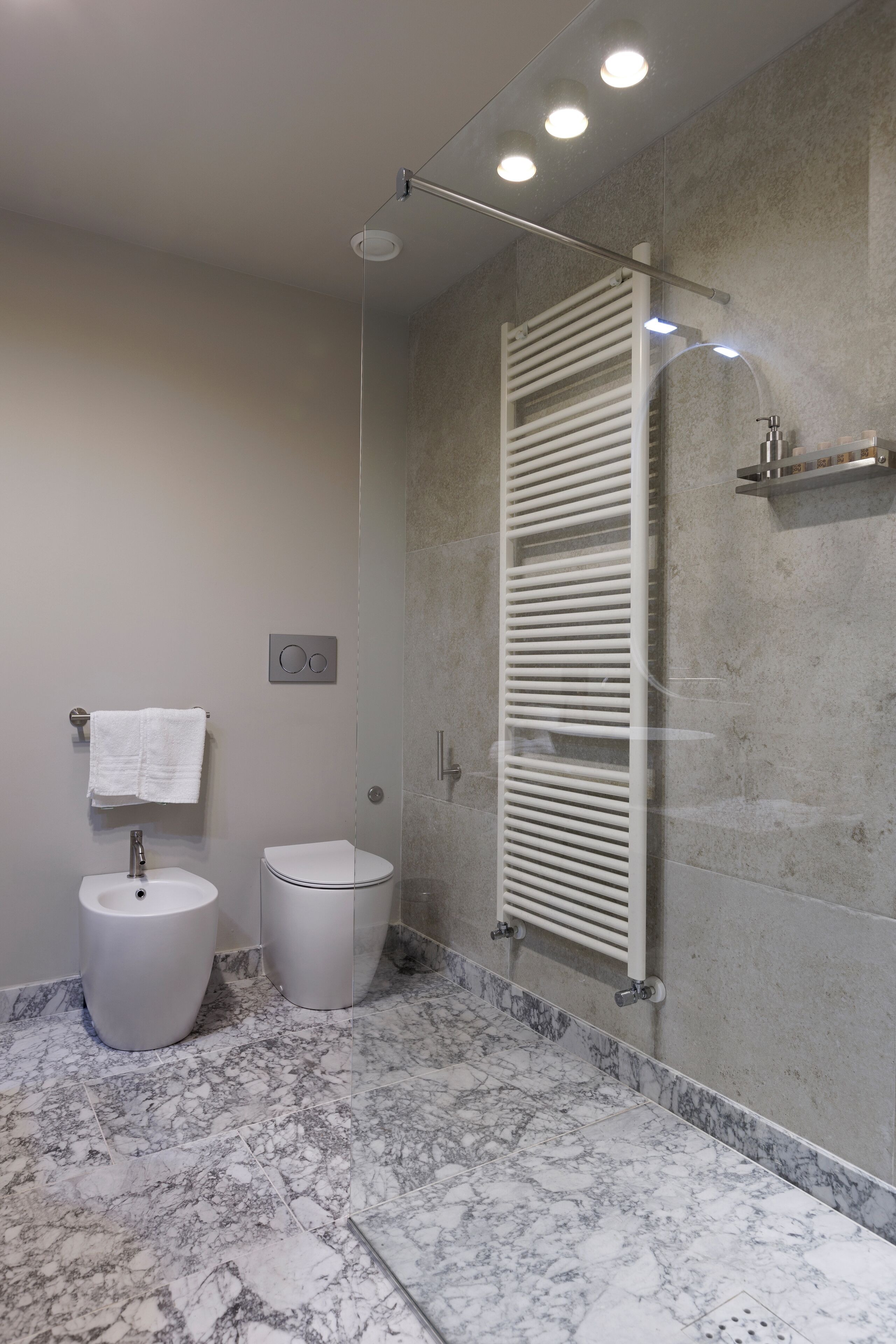 Un baño moderno con suelo de mármol, inodoro, bidé, toallero y cabina de ducha con paredes de vidrio.