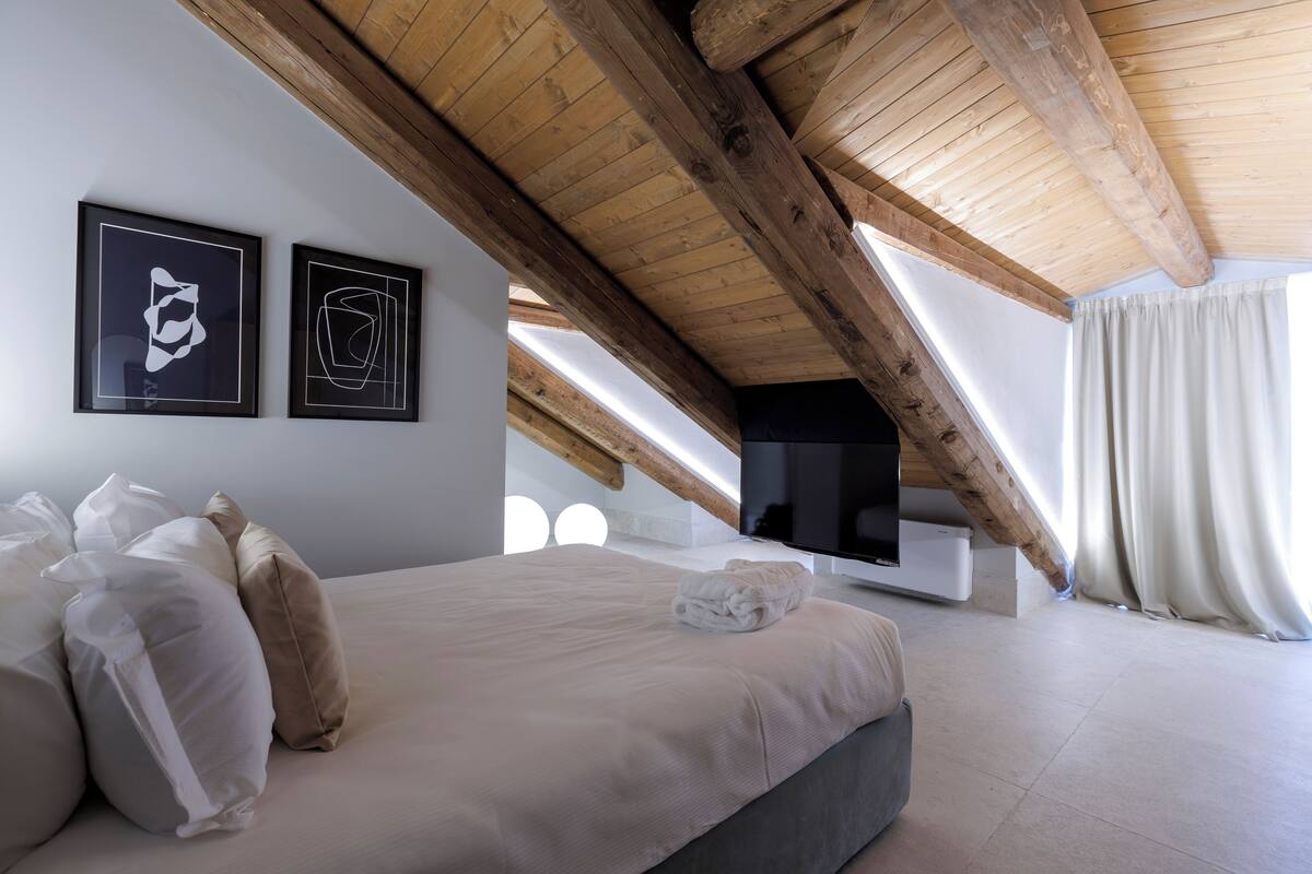 Un dormitorio con una cama grande, un televisor de pantalla plana y vigas de madera en el techo.