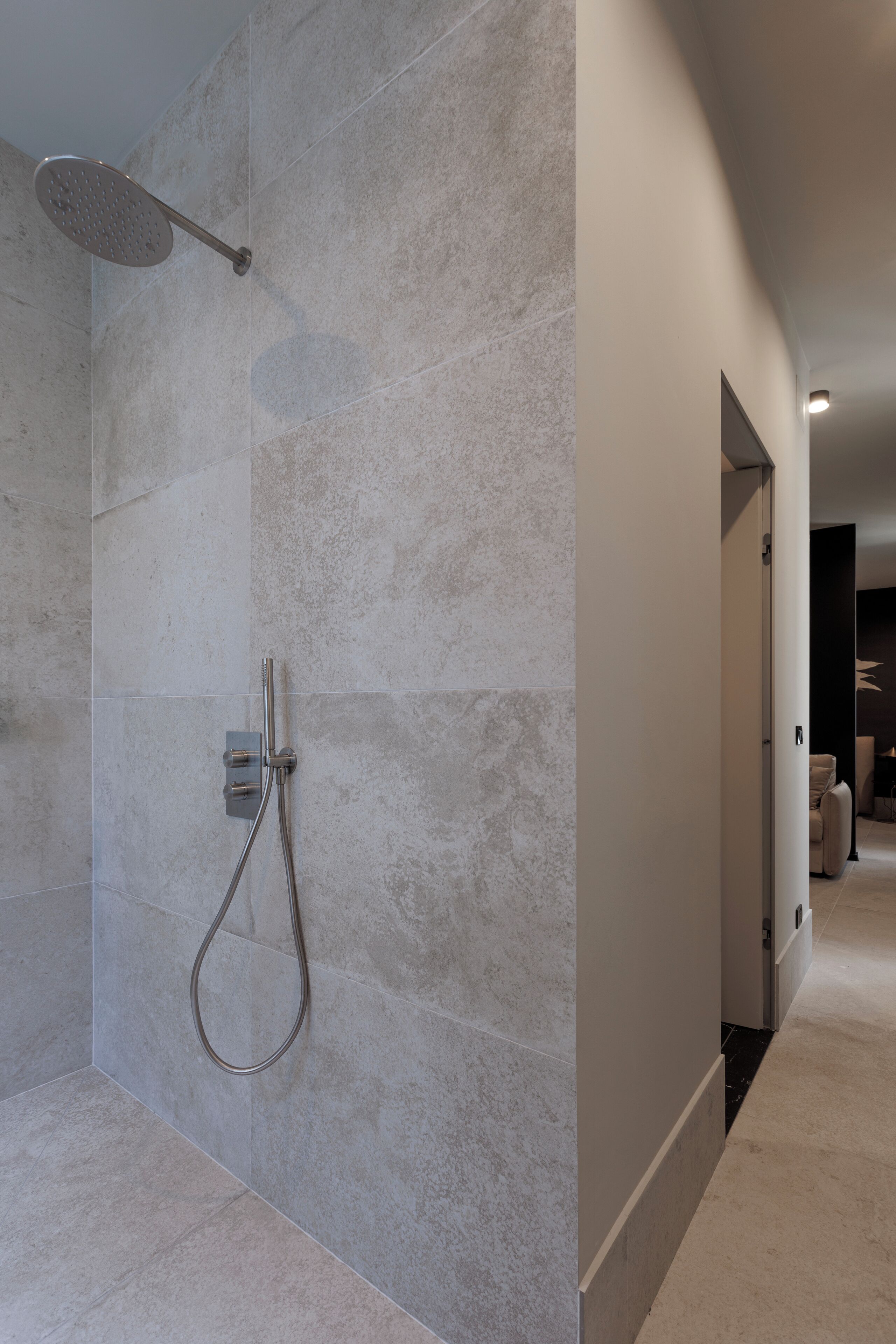 A modern bathroom with a shower, tiled walls, and a hallway leading to another room.