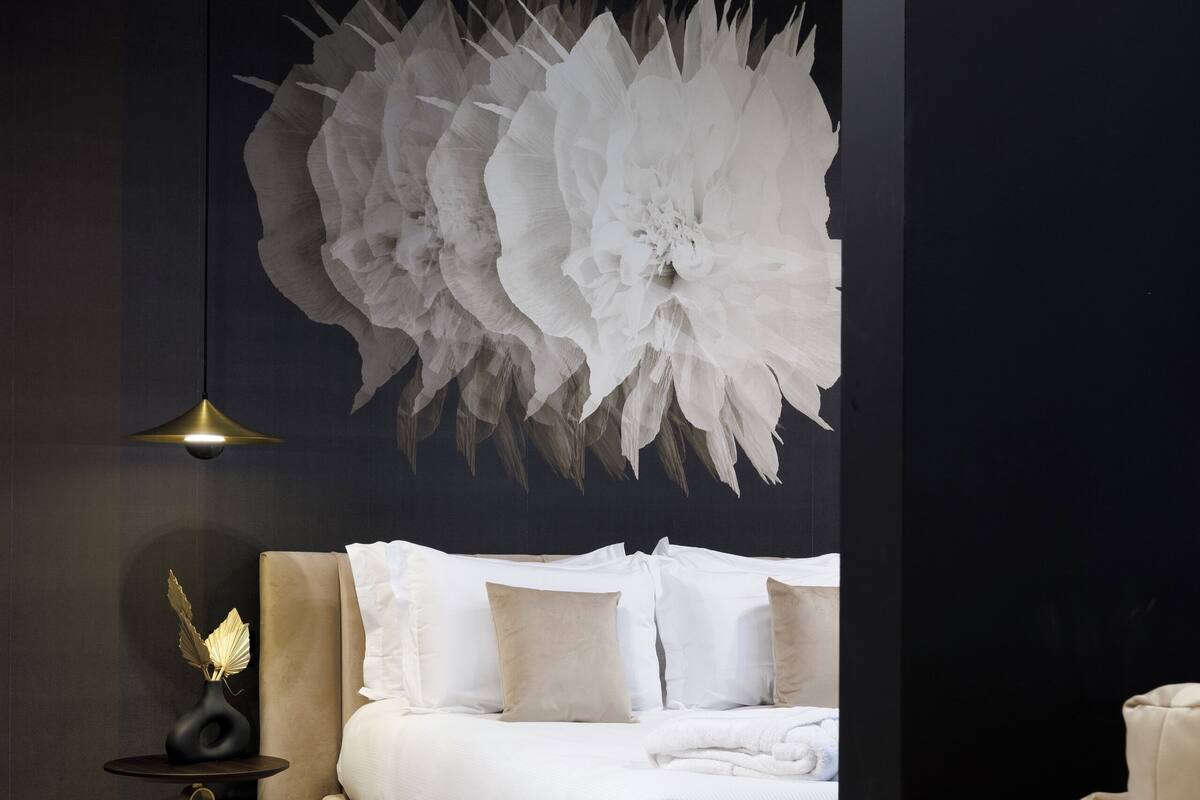Un dormitorio moderno con una cama grande, un elemento decorativo en la pared, una lámpara de pie y una mesita de noche.