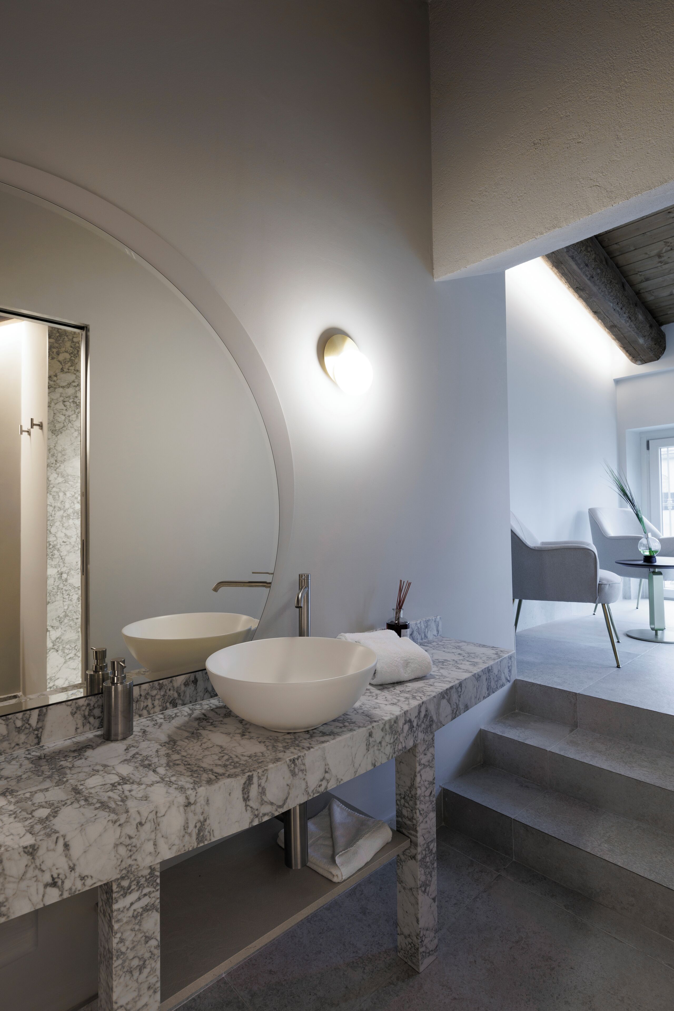 A modern bathroom with a large curved mirror, two sinks, and a marble countertop.