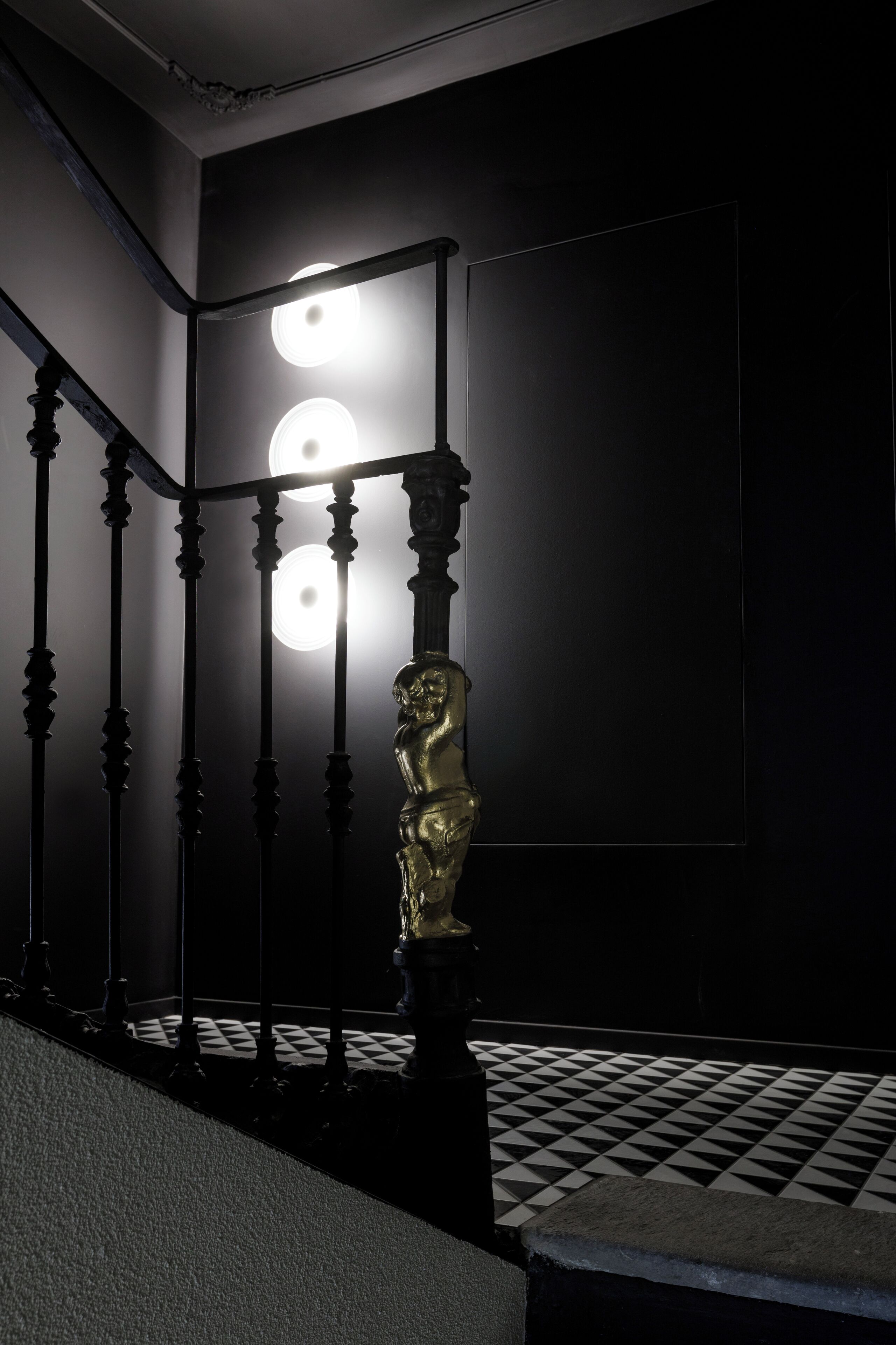 A staircase with a black and white checkered floor, a dark wall, and a light fixture above.