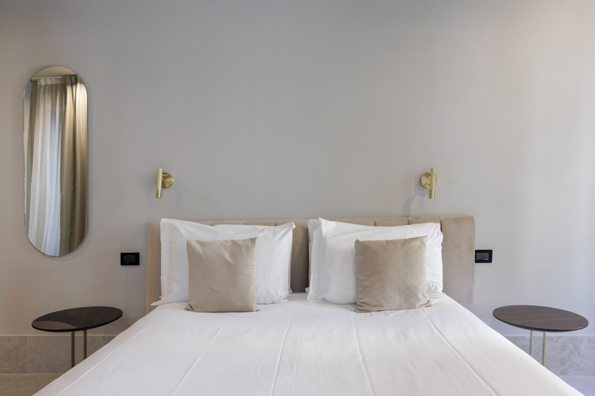 A hotel room with a large bed, two bedside tables, and a wall-mounted mirror.