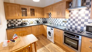 A compact kitchen with wooden cabinets, a washing machine, an oven, and a coffee station.