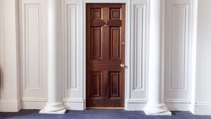 A wooden door with the number 2, flanked by white columns, in a hallway with a carpeted floor.