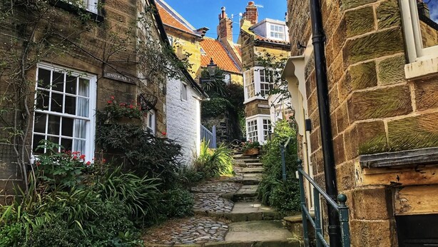 A narrow stone-paved alleyway between buildings with stone facades, a visible staircase, and a sign reading "SUNNY PLACE".