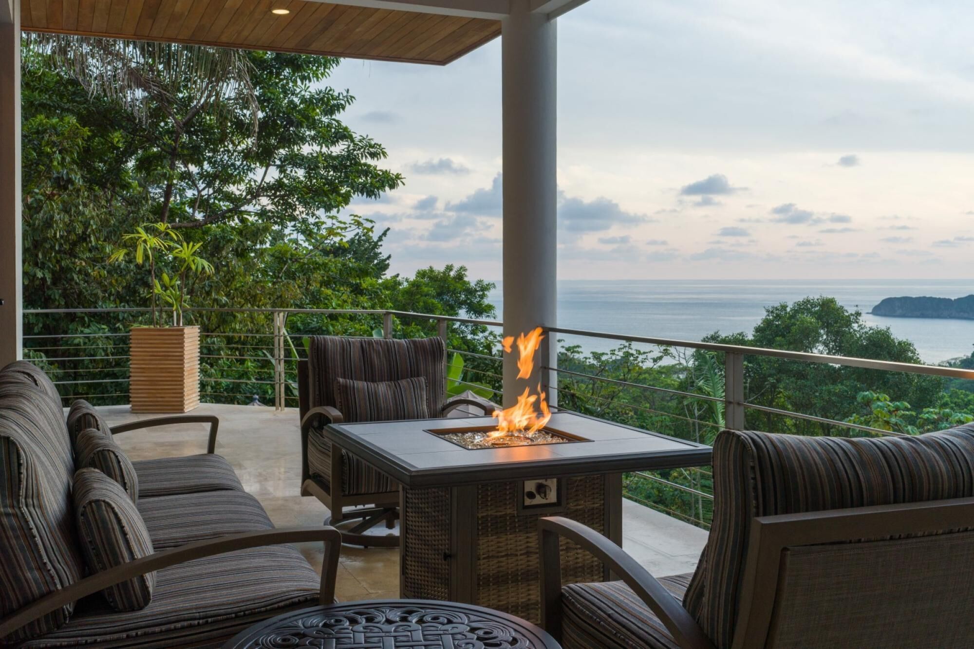 An outdoor seating area with a fire feature, wicker furniture, and a view of the sea.