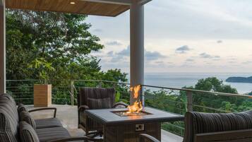 An outdoor seating area with a fire feature, wicker furniture, and a view of the sea.