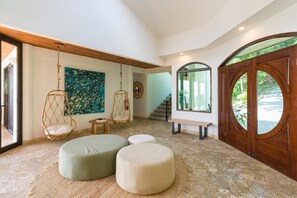 Une pièce spacieuse avec une grande porte en bois, un fauteuil suspendu, un banc et un pouf rond.