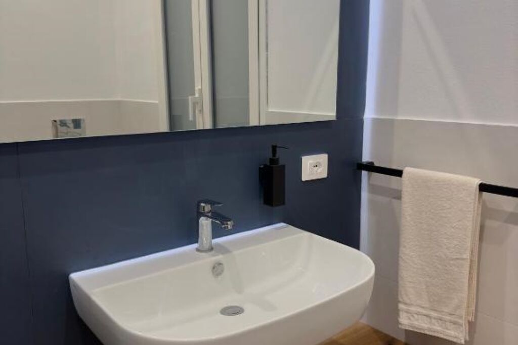Un baño moderno con lavamanos blanco, un espejo y un perchero para toallas.