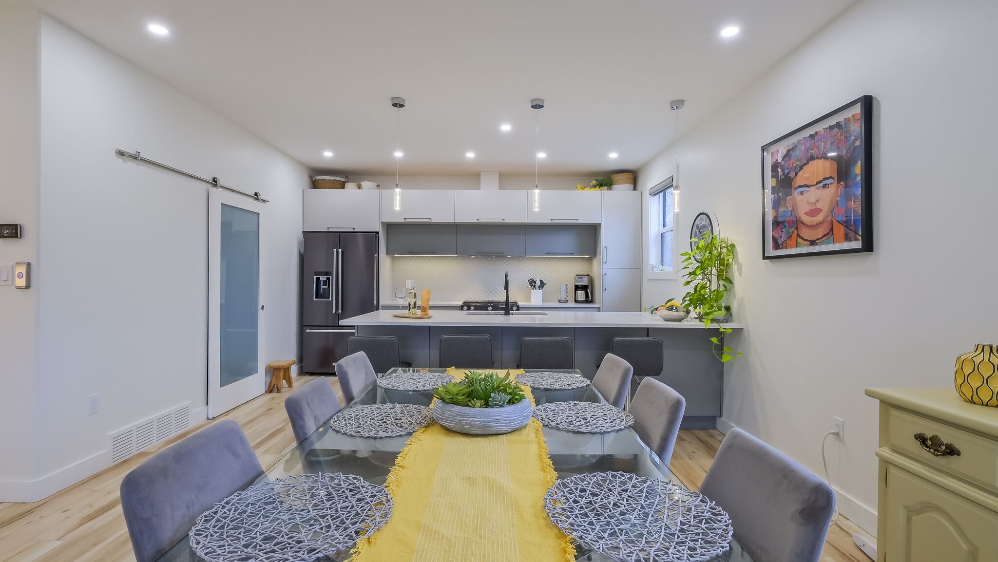Une cuisine moderne dotée d’un îlot central, de meubles de couleur grise et d’un coin repas avec une table en verre et des chaises grises recouvertes de tissu.