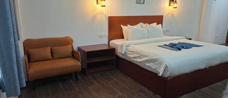 A hotel room with a bed, a brown armchair, a nightstand, and two wall-mounted lights.