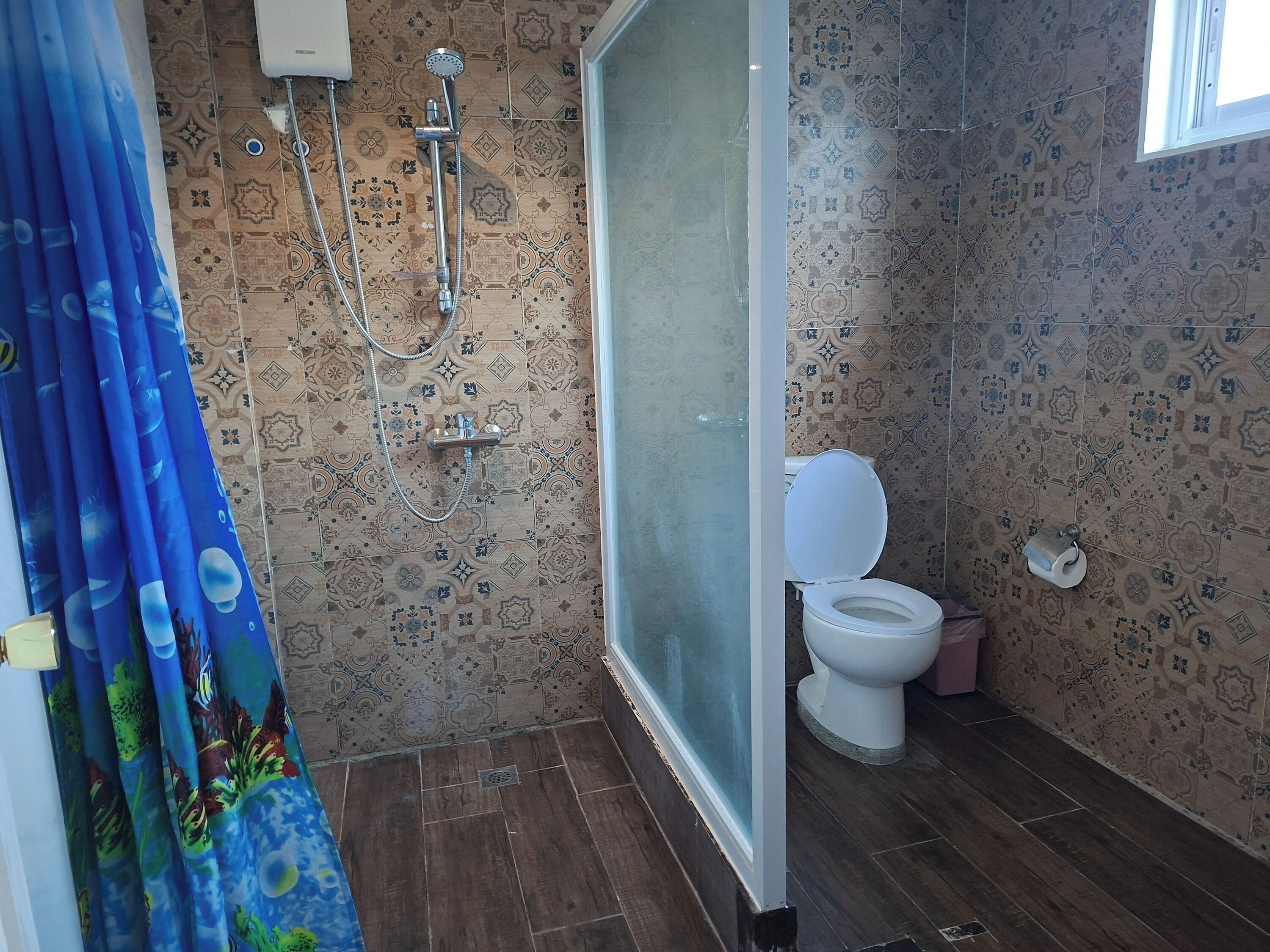 A bathroom with patterned tiles, a shower, a toilet, and a window.