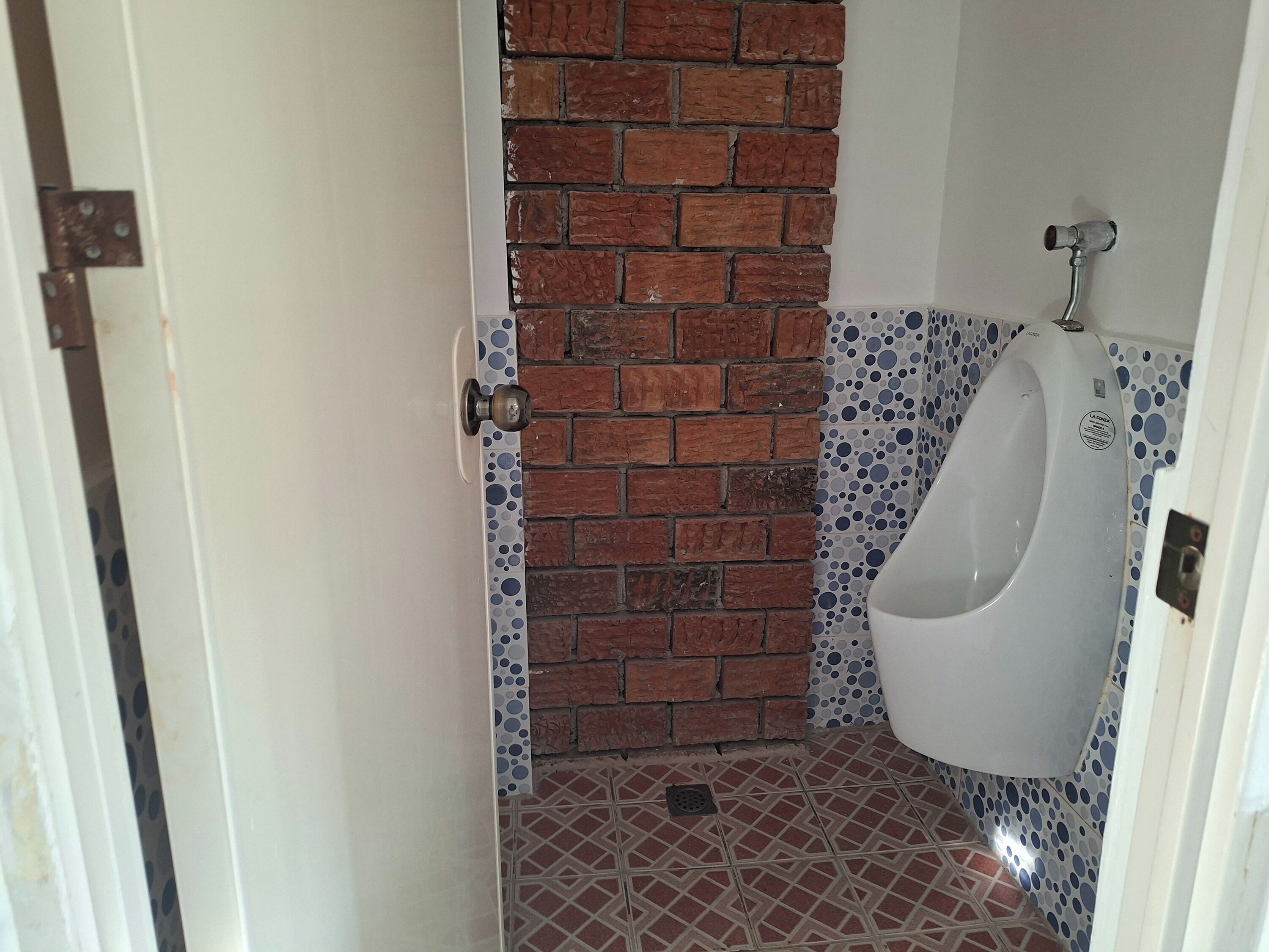 Des toilettes pour hommes avec un urinoir, un mur en briques et des carreaux décoratifs.