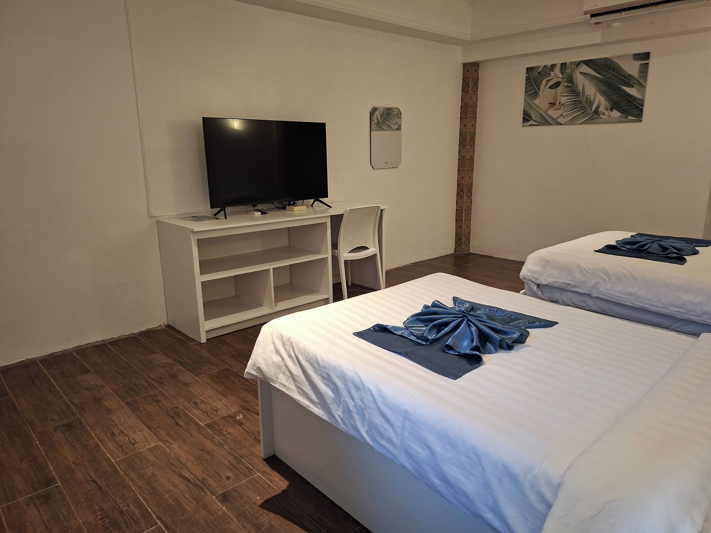 Habitación de hotel con dos camas, un televisor sobre un mueble, una silla y un cuadro en la pared.