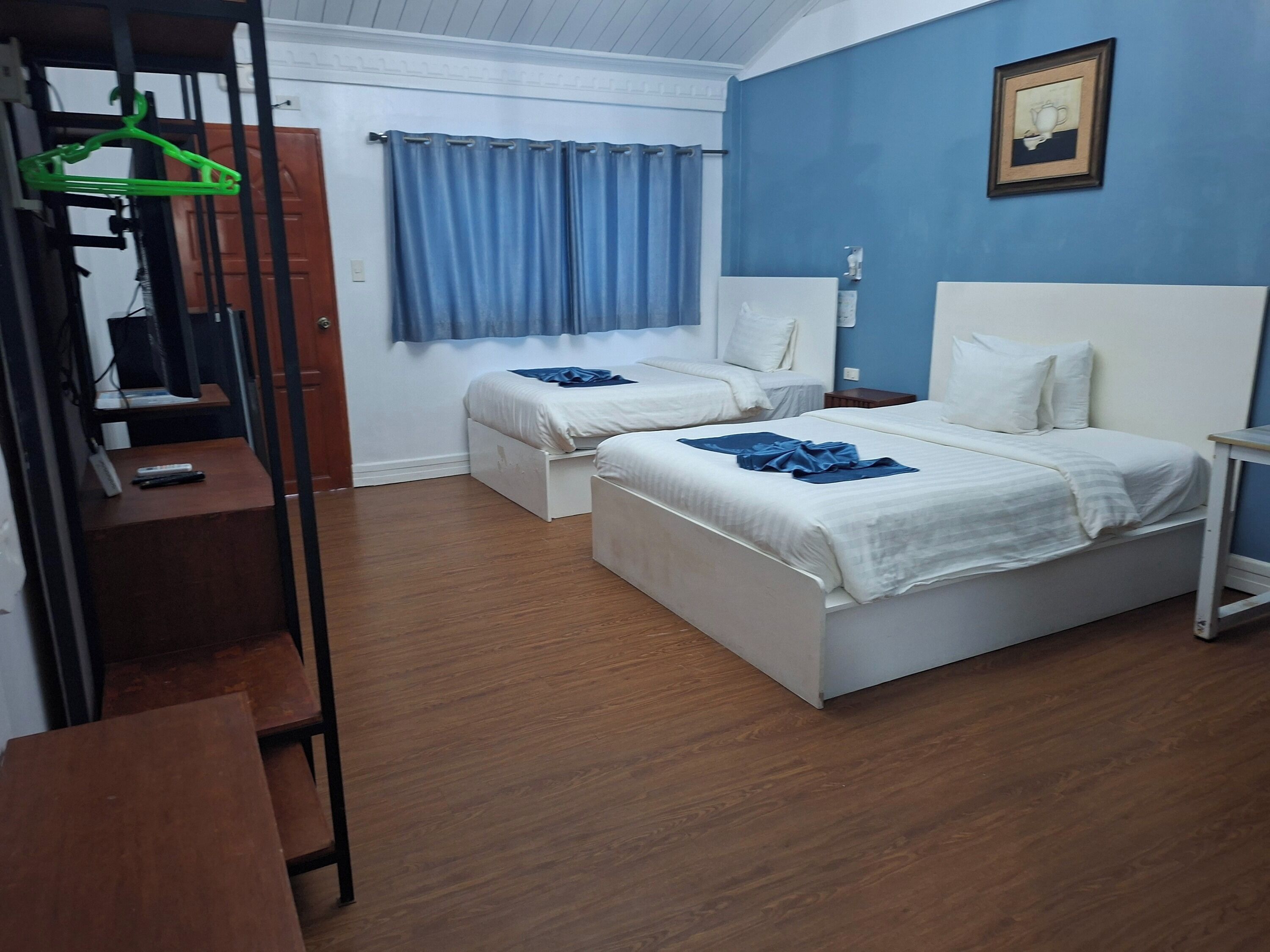 Une chambre avec deux lits, un bureau, une chaise, un portant à vêtements et une fenêtre avec des rideaux.