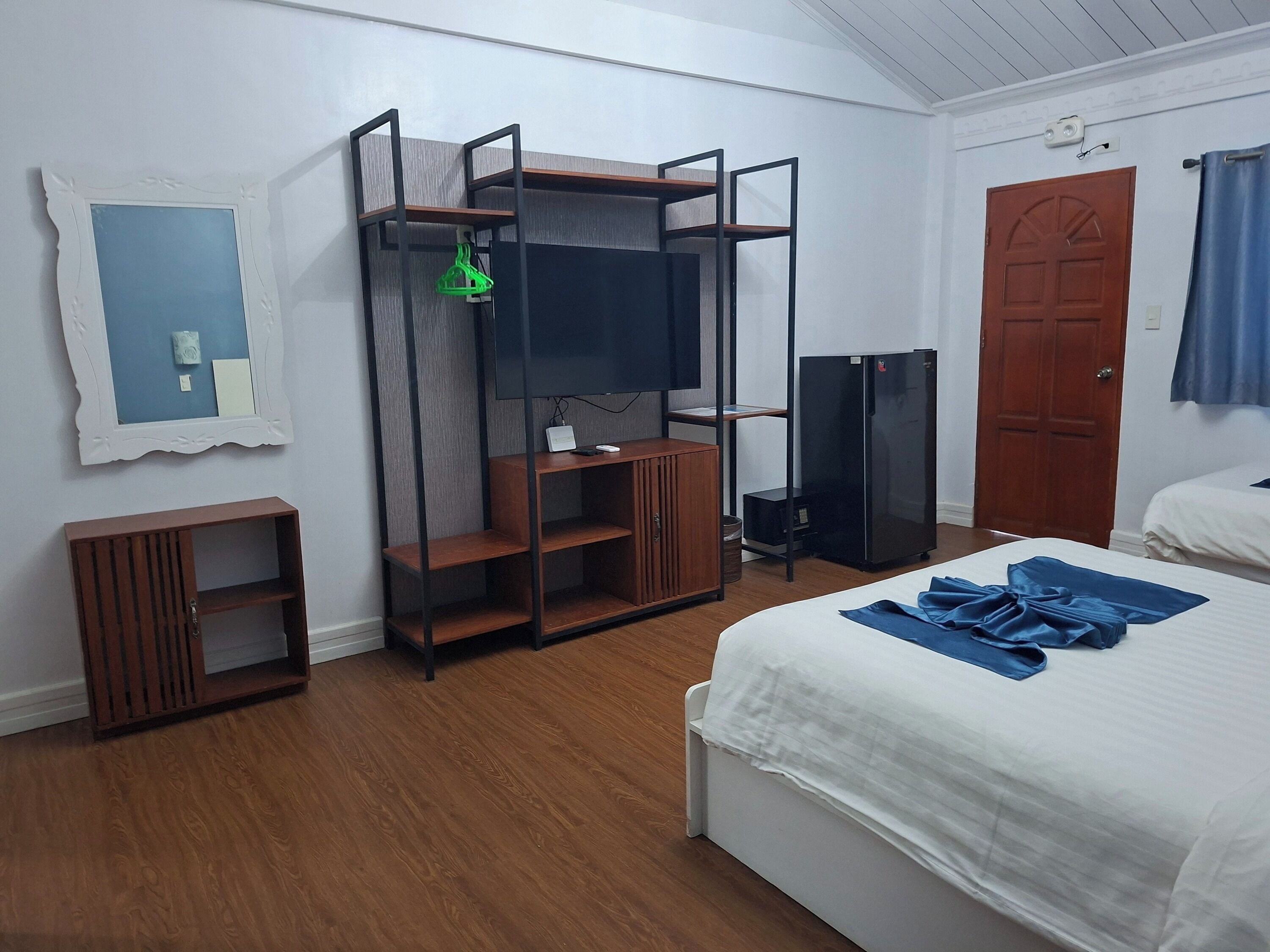A hotel room with a bed, a TV on a wooden stand, a door, and a small wooden cabinet.
