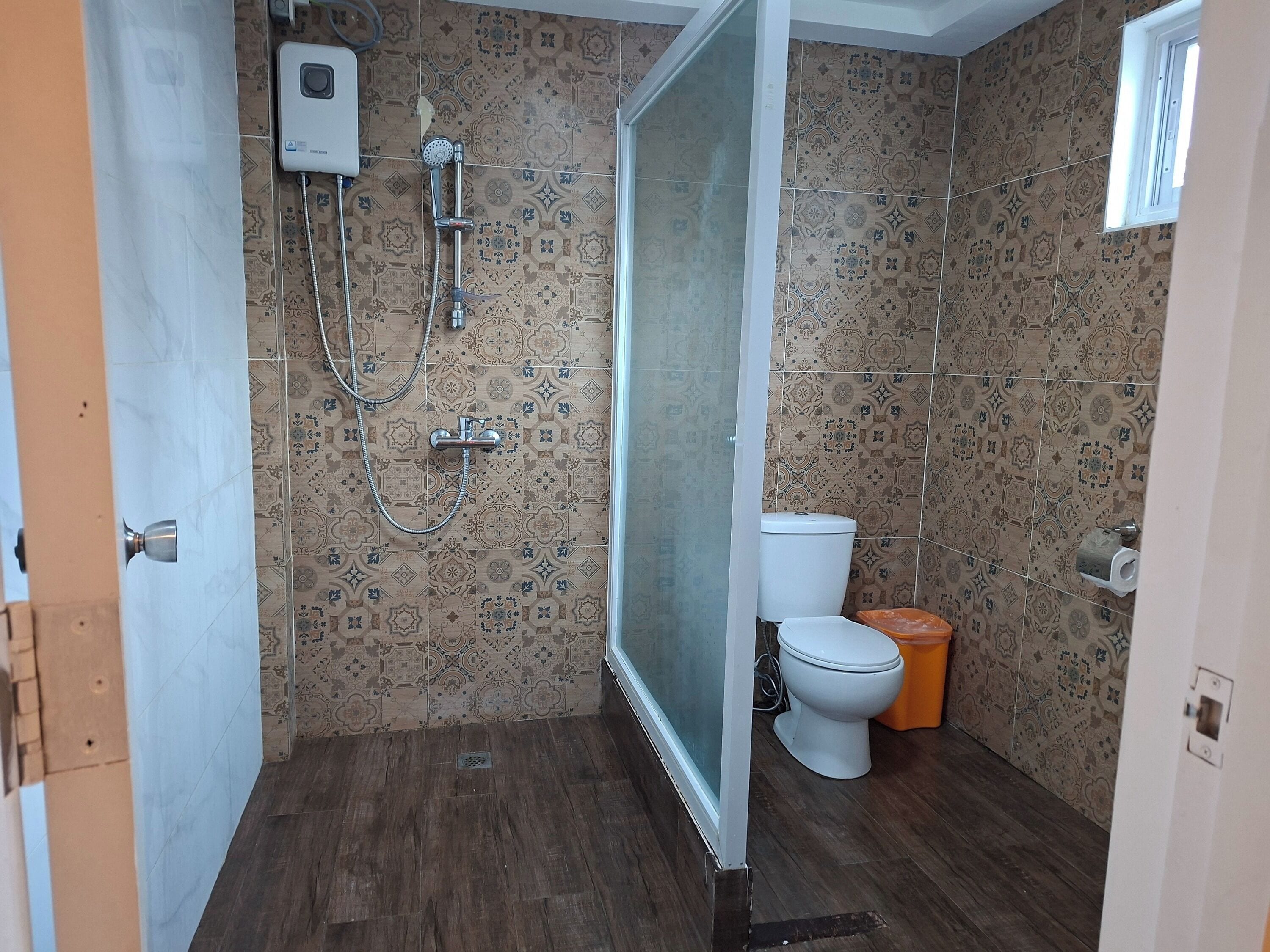 A bathroom with patterned tiles, a shower, a toilet, and a window.