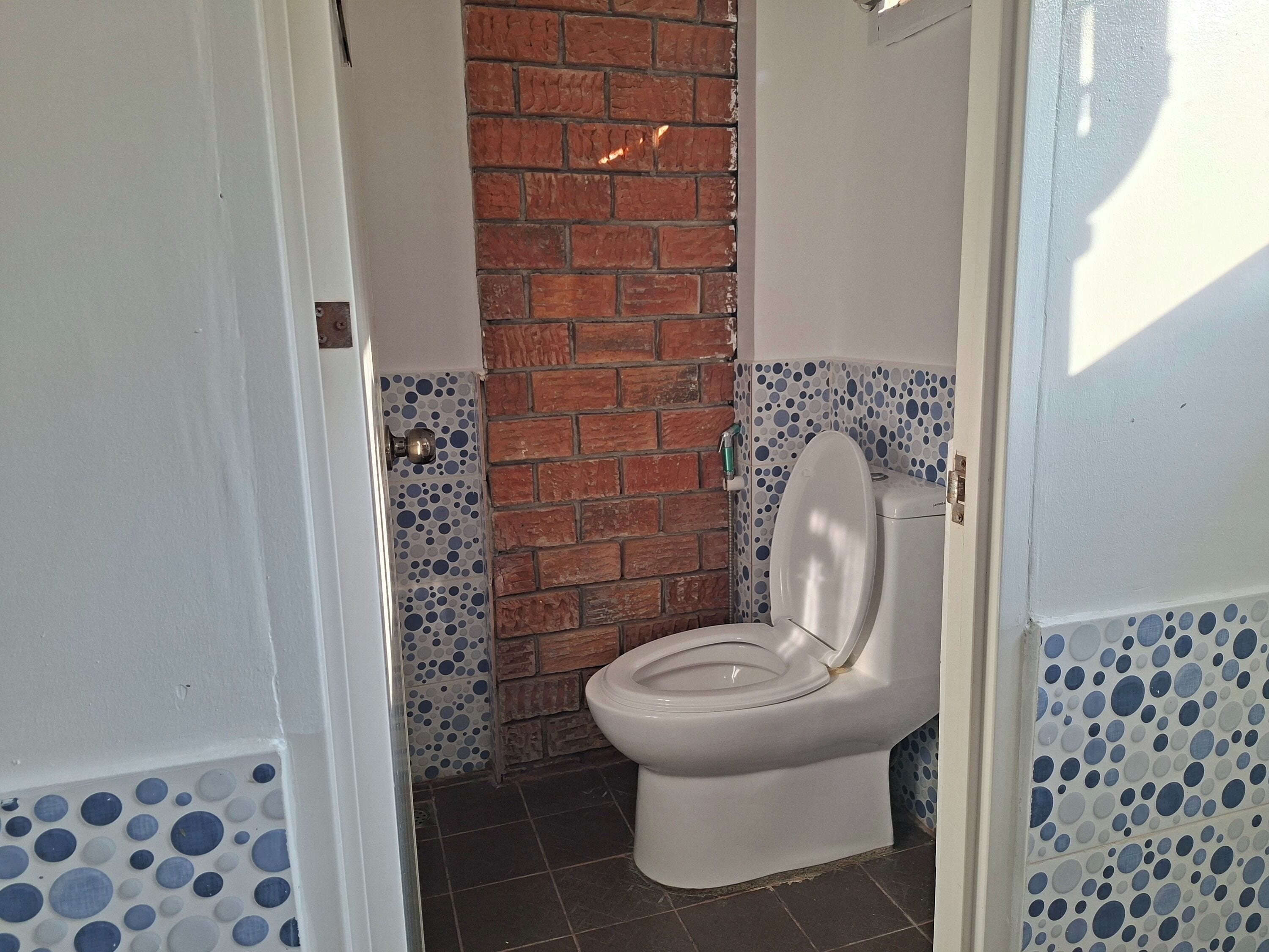 Baño con inodoro blanco, pared de ladrillo y paredes con azulejos azules y blancos.