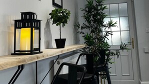 Een gang met een houten bankje, een potplant, een lijst met foto en een wandlamp.