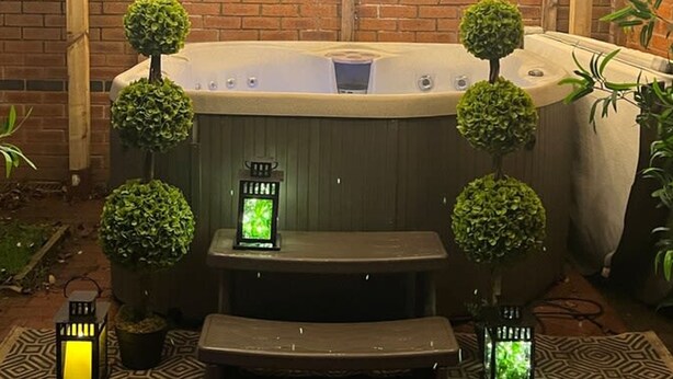 Een hottub onder een houten pergola, omgeven door bakstenen muren en potplanten.