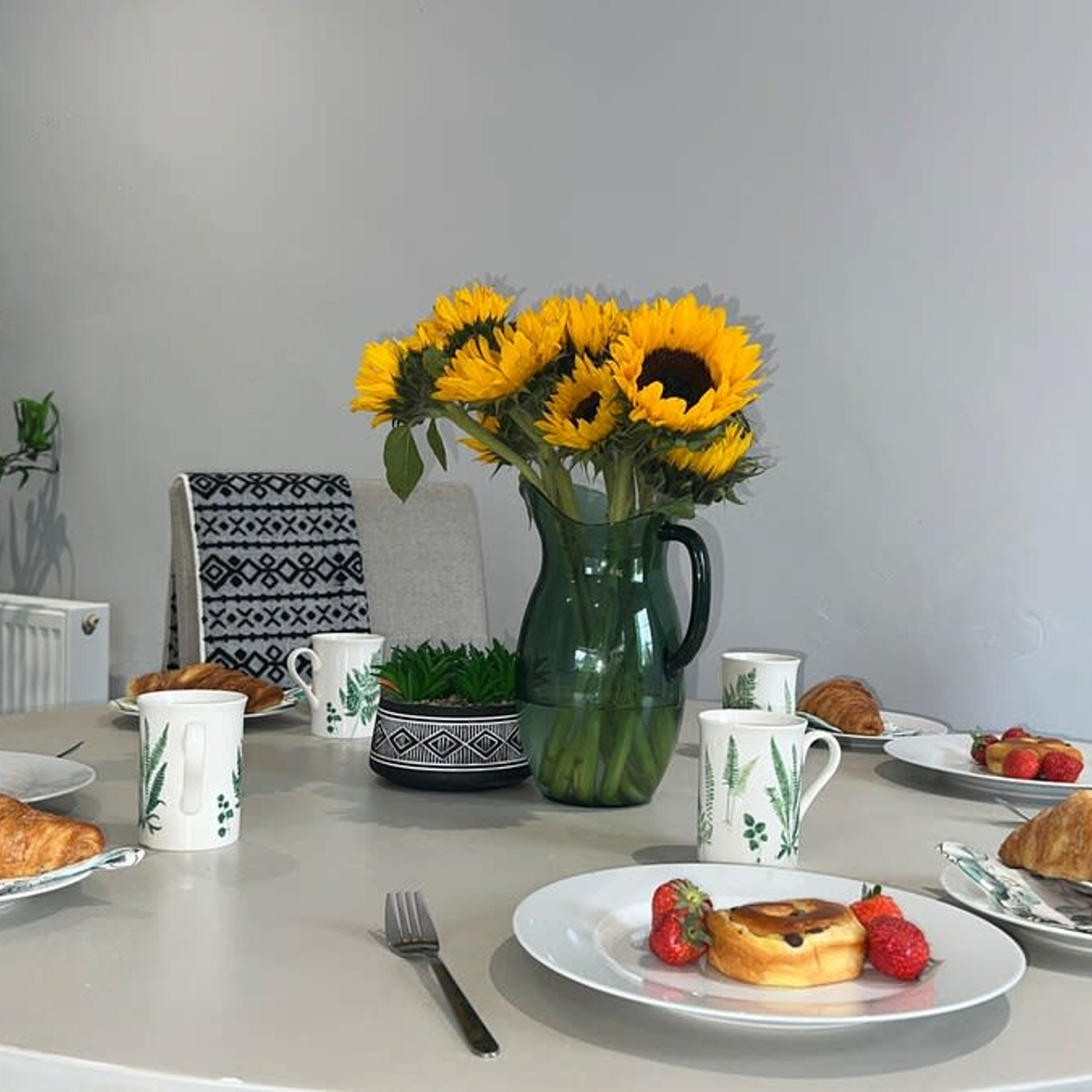 Een eettafel met een vaas zonnebloemen, een theepot en borden met eten en drinken.