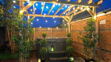 A covered outdoor area with a brick wall, wooden pergola, string lights, and potted plants.
