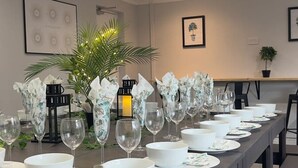 Een eettafel gedekt met witte borden, kommen en wijnglazen, omringd door decoratieve vazen en een potplant.