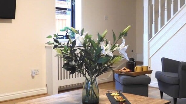 A living room with a wooden coffee table, a vase with flowers, a sofa, and a staircase. - Lion House Chester - Very Near Zoo Ideal for Families (Chester)