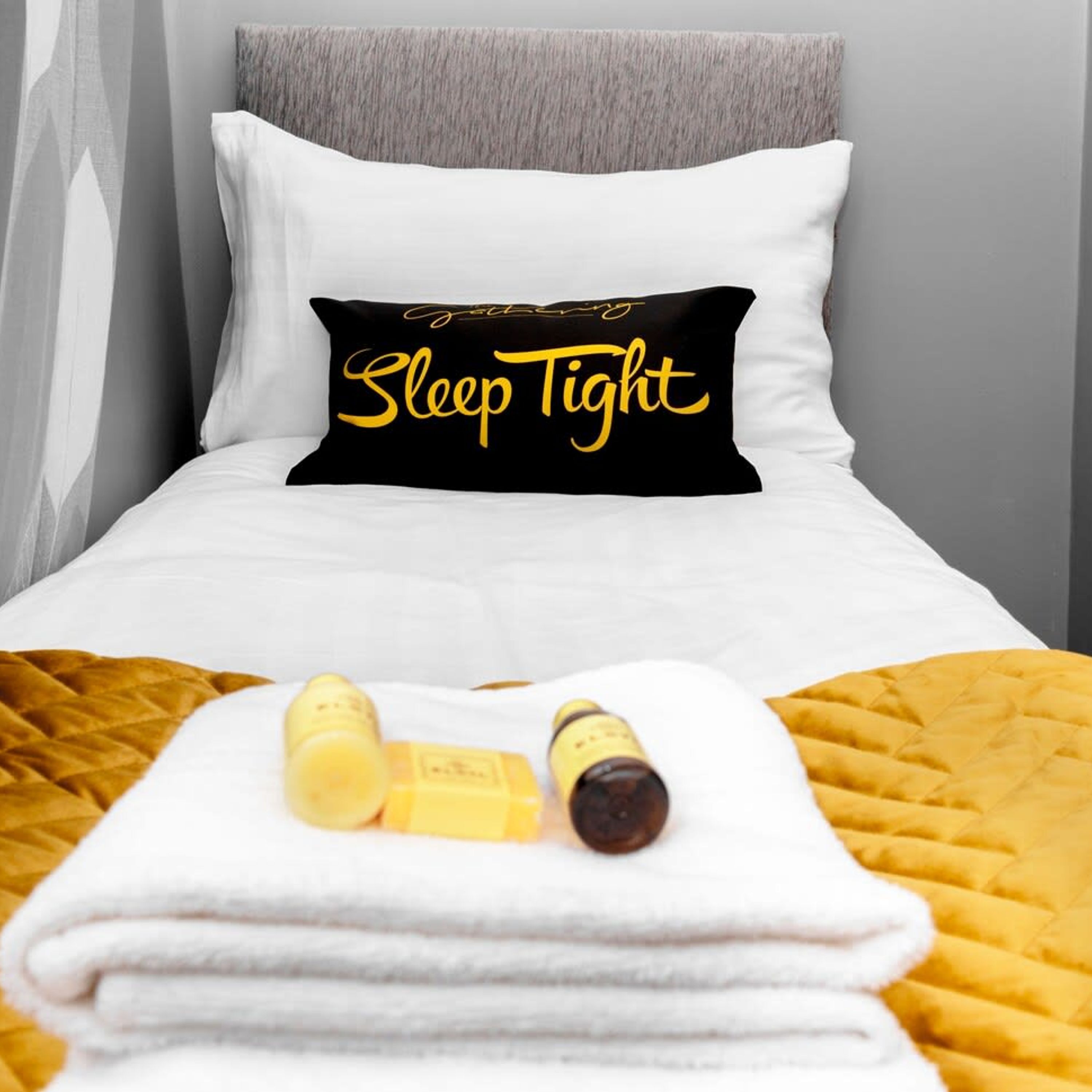 Ein Bett mit einem Kissen, auf dem 'Schlaf gut' steht, und zwei Flaschen auf einem gefalteten weißen Handtuch.