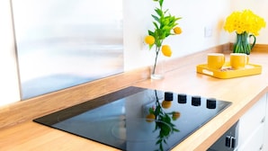A modern kitchen with a black induction cooktop, a wooden countertop, a vase with yellow flowers, and two yellow cups on a tray. - The Kings Gathering - Very Central Chester (Chester)