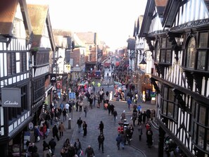 A bustling street scene with traditional half-timbered buildings, cobblestone pavement, and a crowd of people. - The Kings Gathering - Very Central Chester (Chester)