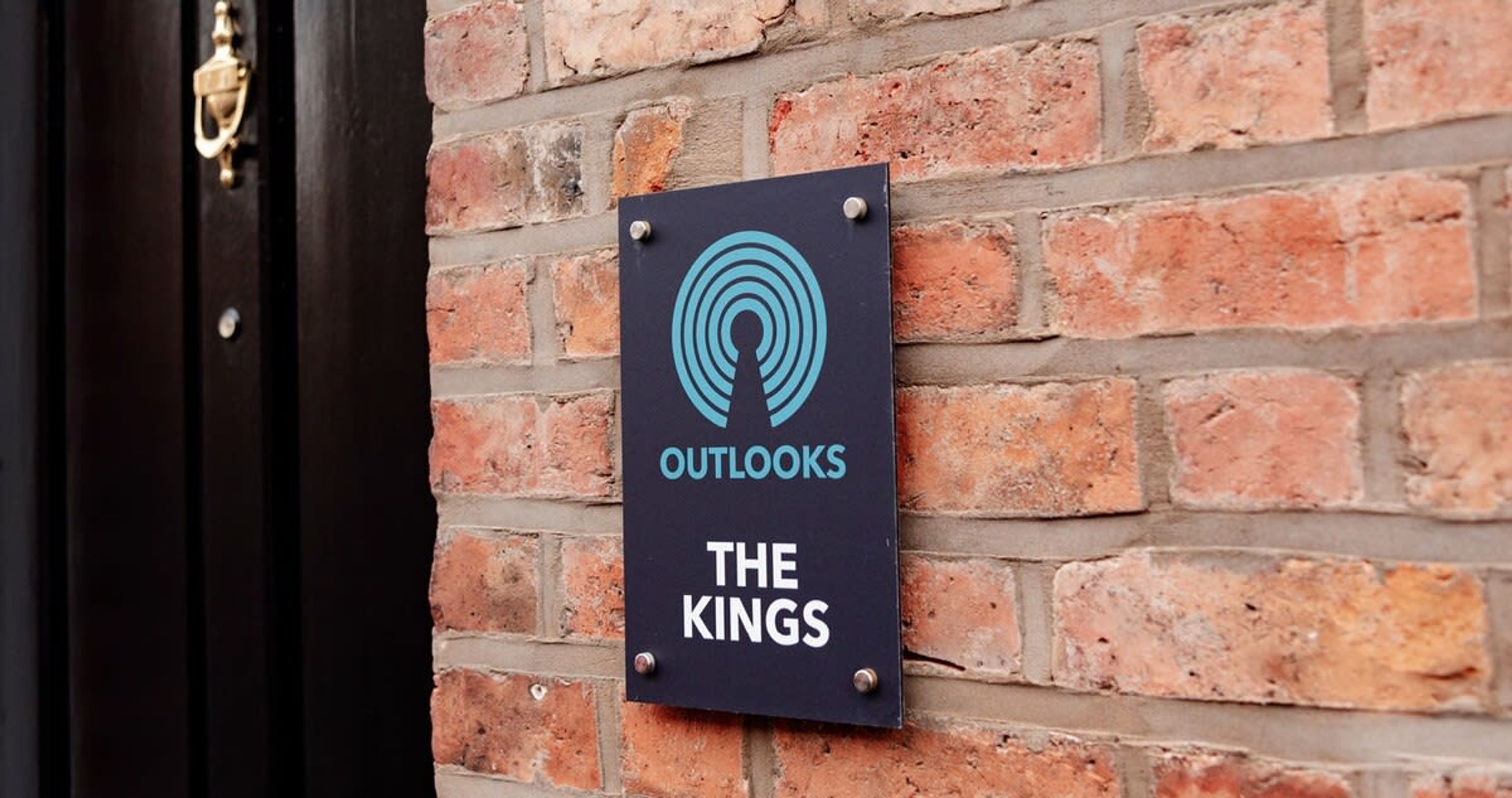 A sign on a brick wall with the words 'OUTLOOKS THE KINGS' and a logo.